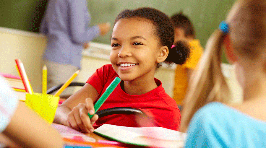 Image of smiling girl in a classroom, holding a crayon