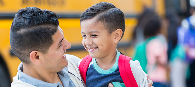 Image of father and son hugging in front of a schoolbus