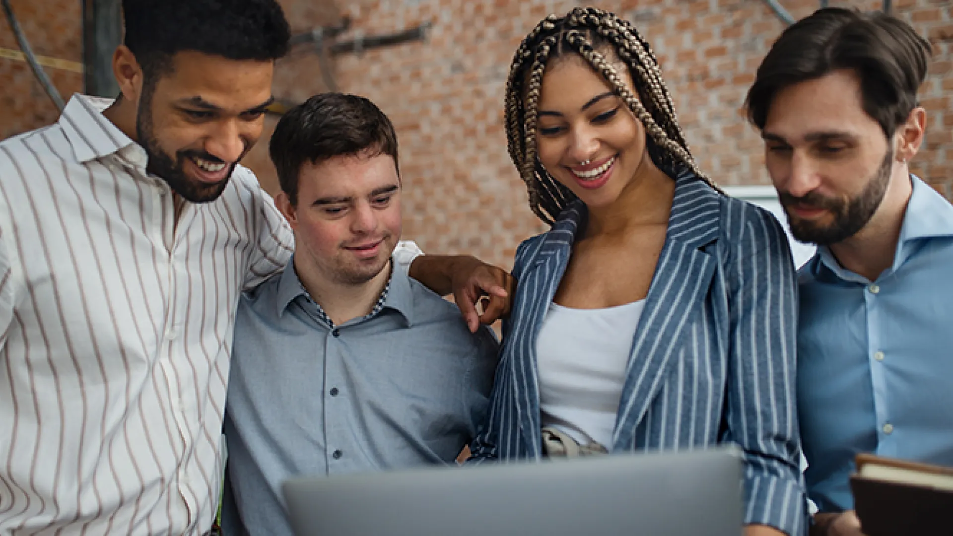 Cheerful young businesspeople with laptop working in office, social inclusion and cooperation