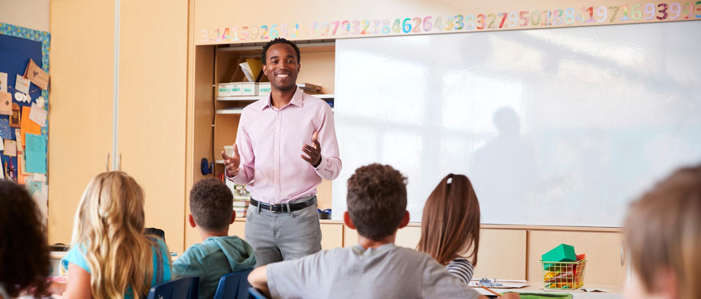 Black teacher providing instruction at front of middle school classroom with students listening