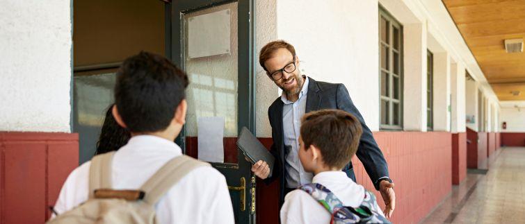 educator greets middle school students outside a classroom door