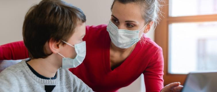 teacher and student wearing masks and talking while looking at a laptop