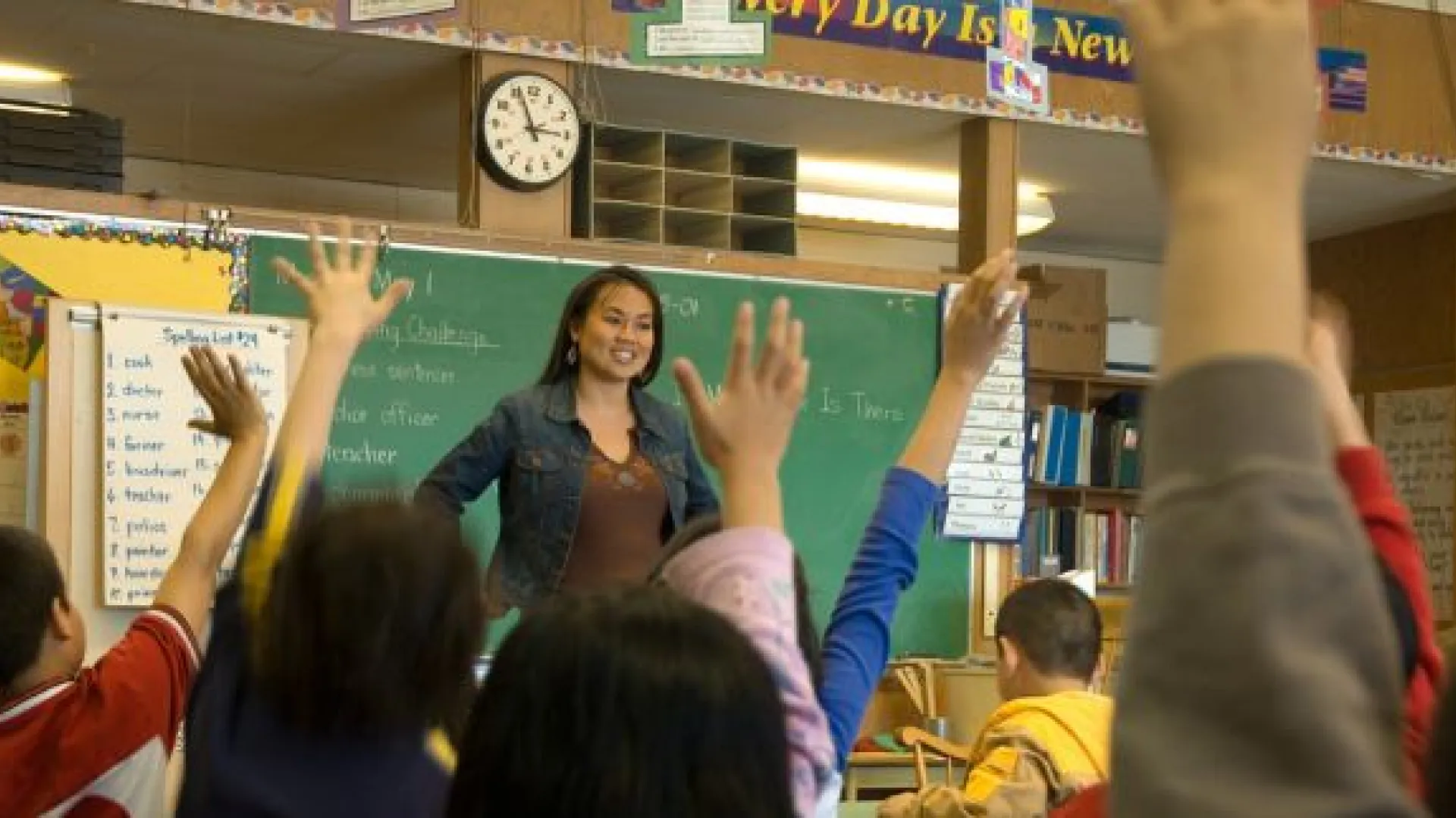 teacher standing at front of middle school classroom with students raising their hands