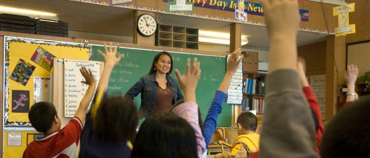 teacher standing at front of middle school classroom with students raising their hands