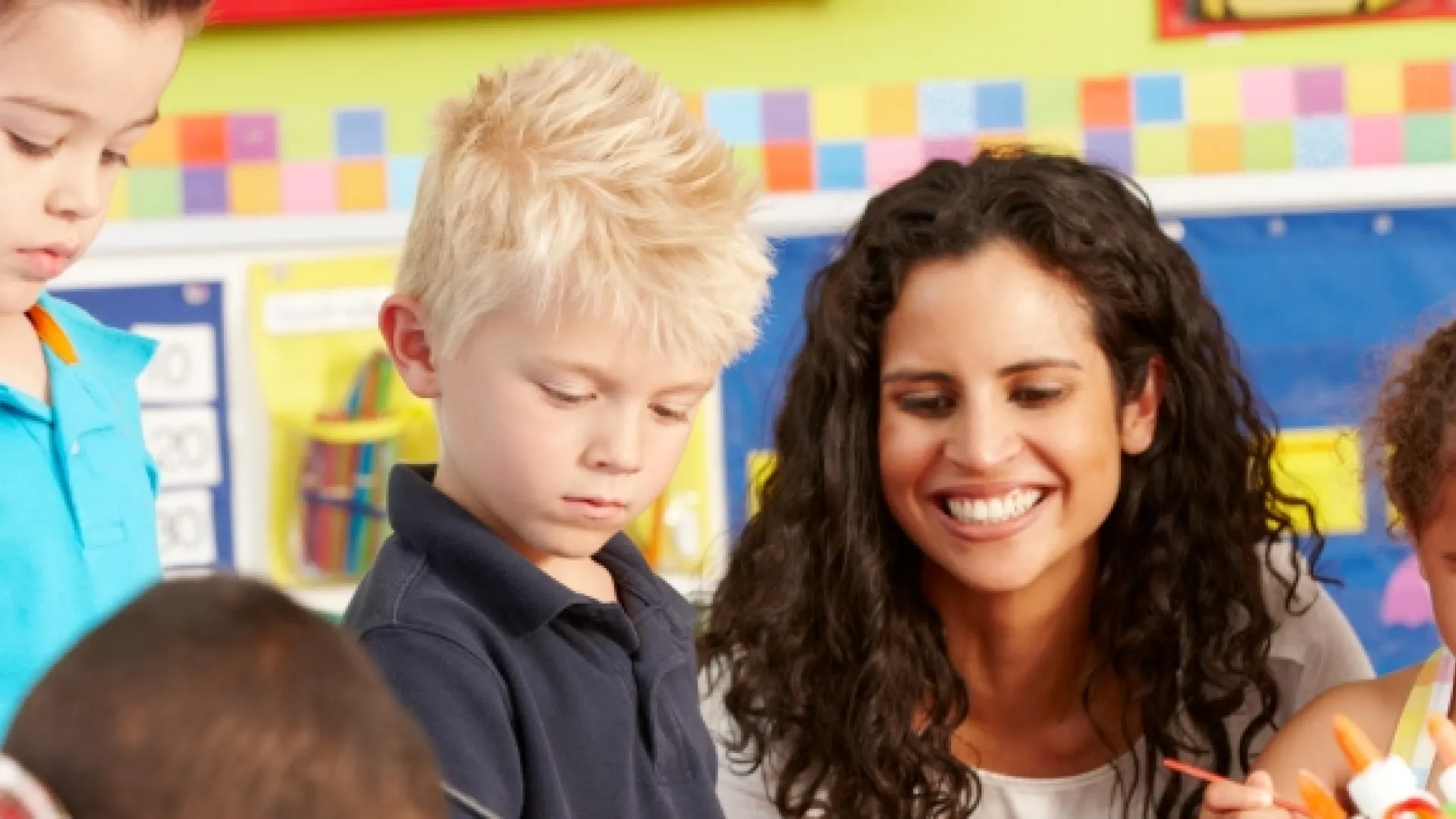 Female teacher helping four preschool students paint