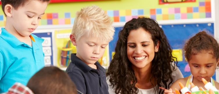 Female teacher helping four preschool students paint