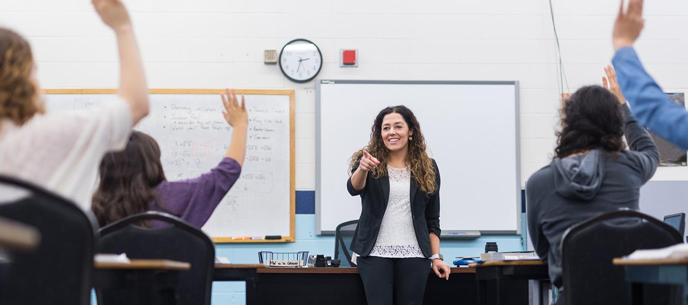 Teacher standing at front of classroom with students hands raised