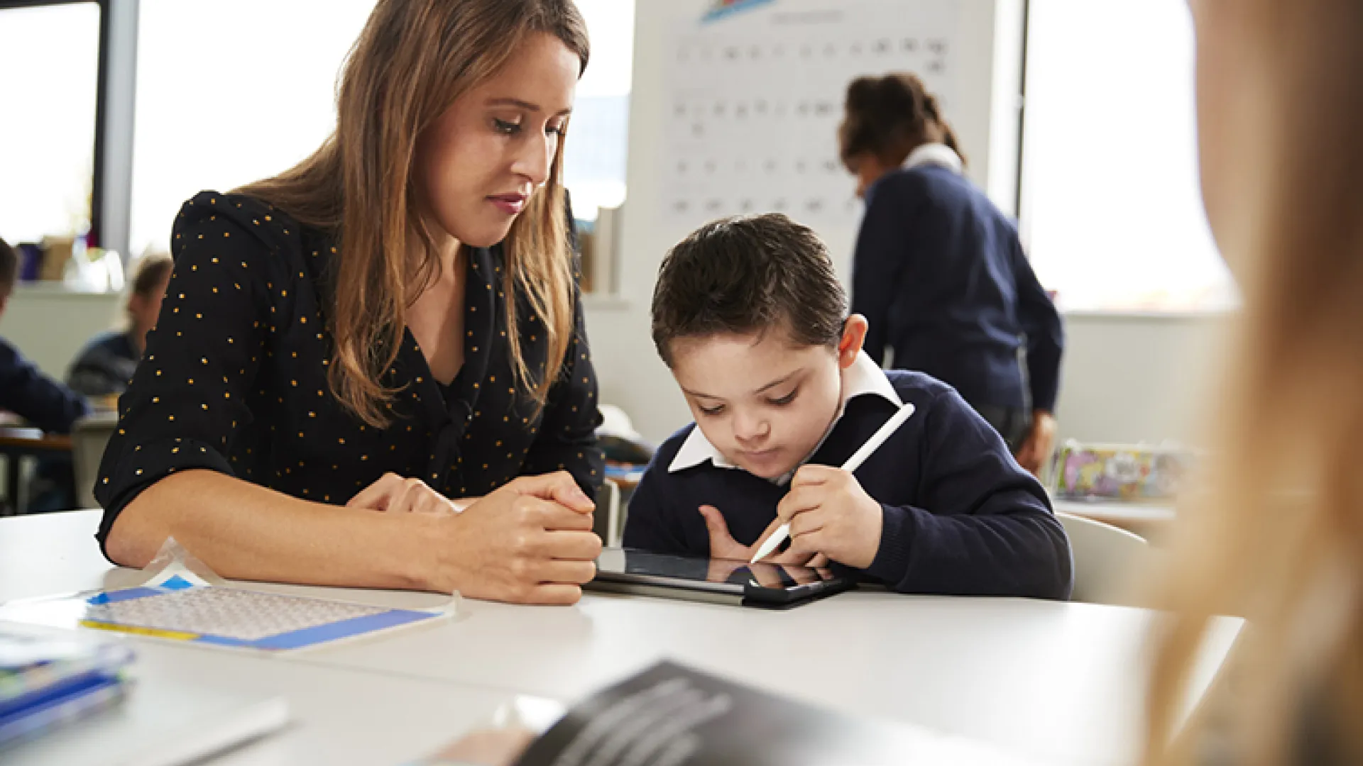 female teacher working with young student on tablet