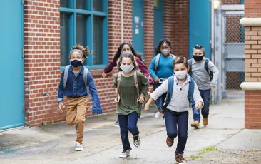 Image of kids running outside school, wearing masks
