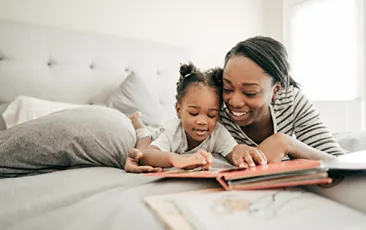 Image of mother with young girl reading on bed together