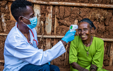 Male doctor taking senior woman temperature in remote village, East Africa 