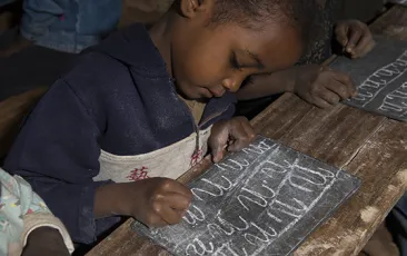 African boy writing with chalk on slate