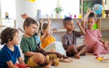 Preschool children seated in a circle raising hands