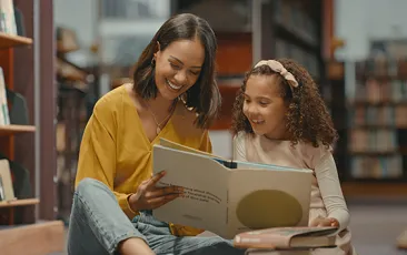 Mother and daughter reading together in library