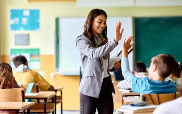 Happy elementary school teacher giving high five to her student during class in the classroom