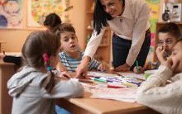 Happy preschool teacher assisting children with their drawings