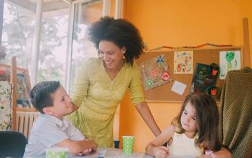 teacher standing by two elementary students seated at a table