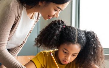 teacher standing over a middle school student writing in a notebook