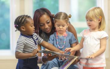 Teacher reading a book with three female toddlers