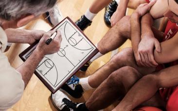 Basketball team and coaching examining a play on a whiteboard