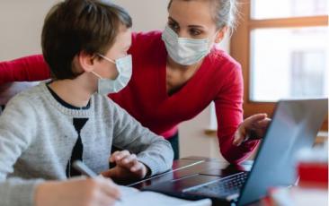 teacher and student wearing masks and talking and pointing at a laptop
