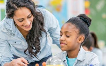 teacher helping high school student seated at a desk with solar system diagram