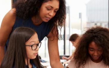 teacher helping two high school students at a desk