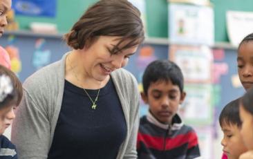 teacher looking at book sitting on floor with elementary students