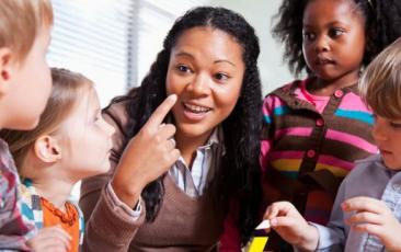 teacher with elementary students smiling and pointing to herself