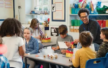 Teacher smiling and talking at tables with elementary students
