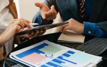 two people looking at tablet and graphs on paper