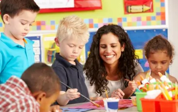 Female teacher helping four preschool students paint