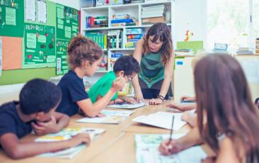 teacher working with four elementary school students at a table 