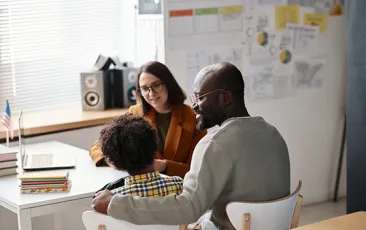Father and young student talking to teacher in classroom