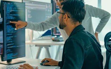 Man with colleague examining code on computer
