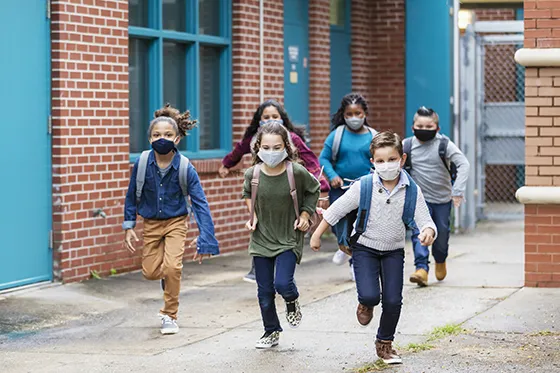 Image of kids running outside school, wearing masks