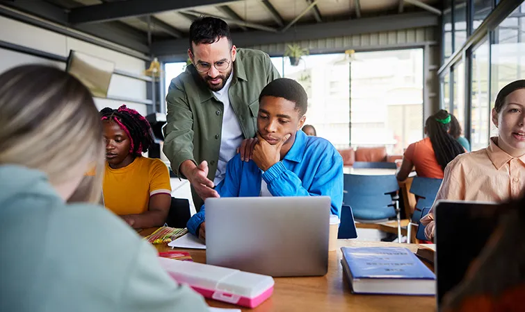 Trainer helping student on laptop in classroom