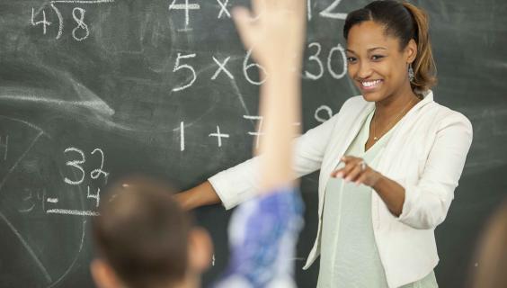 Math teacher at chalkboard with student raising hand