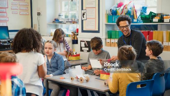 Teacher smiling and talking at tables with elementary students