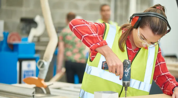 Young woman apprentice using a drill