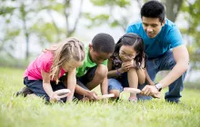 Image of young teacher with students using magnifying glasses outside