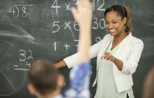 Math teacher at chalkboard with student raising hand
