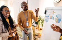 Three people discussing graphs on a board. 