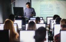 Teacher standing in front of adult class room, each adult is sitting in front of a computer