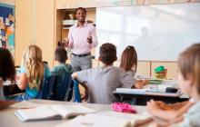 Black teacher providing instruction at front of middle school classroom with students listening