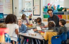 Teacher smiling and talking at tables with elementary students