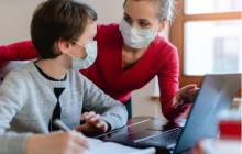 teacher and student wearing masks and talking while looking at a laptop