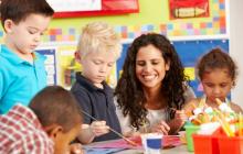 Female teacher helping four preschool students paint