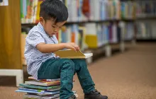 Little boy sitting on books in library