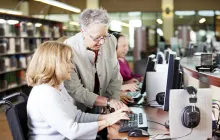 Older library volunteer helping patron